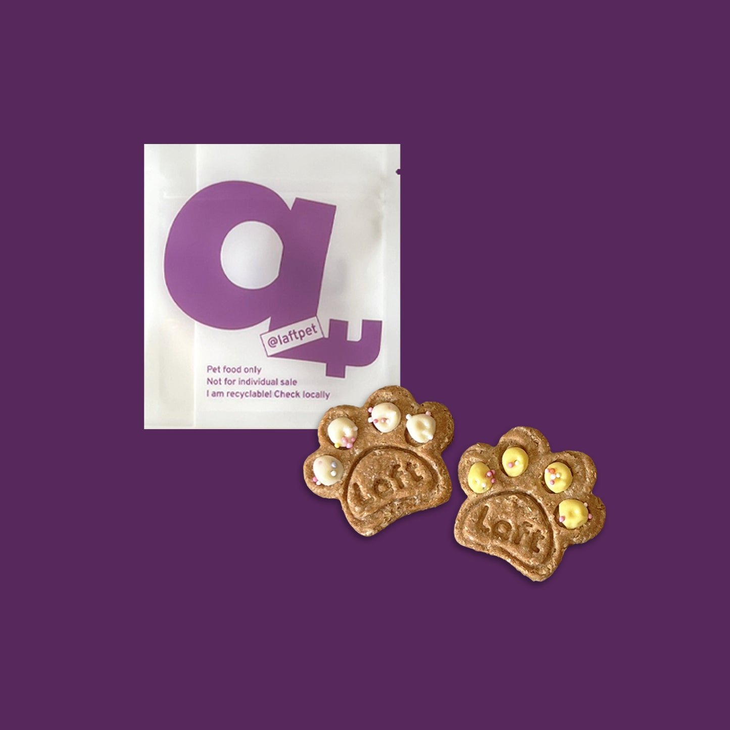 A white Laft Pet treat pouch placed next to two paw cookies on a dark purple background.