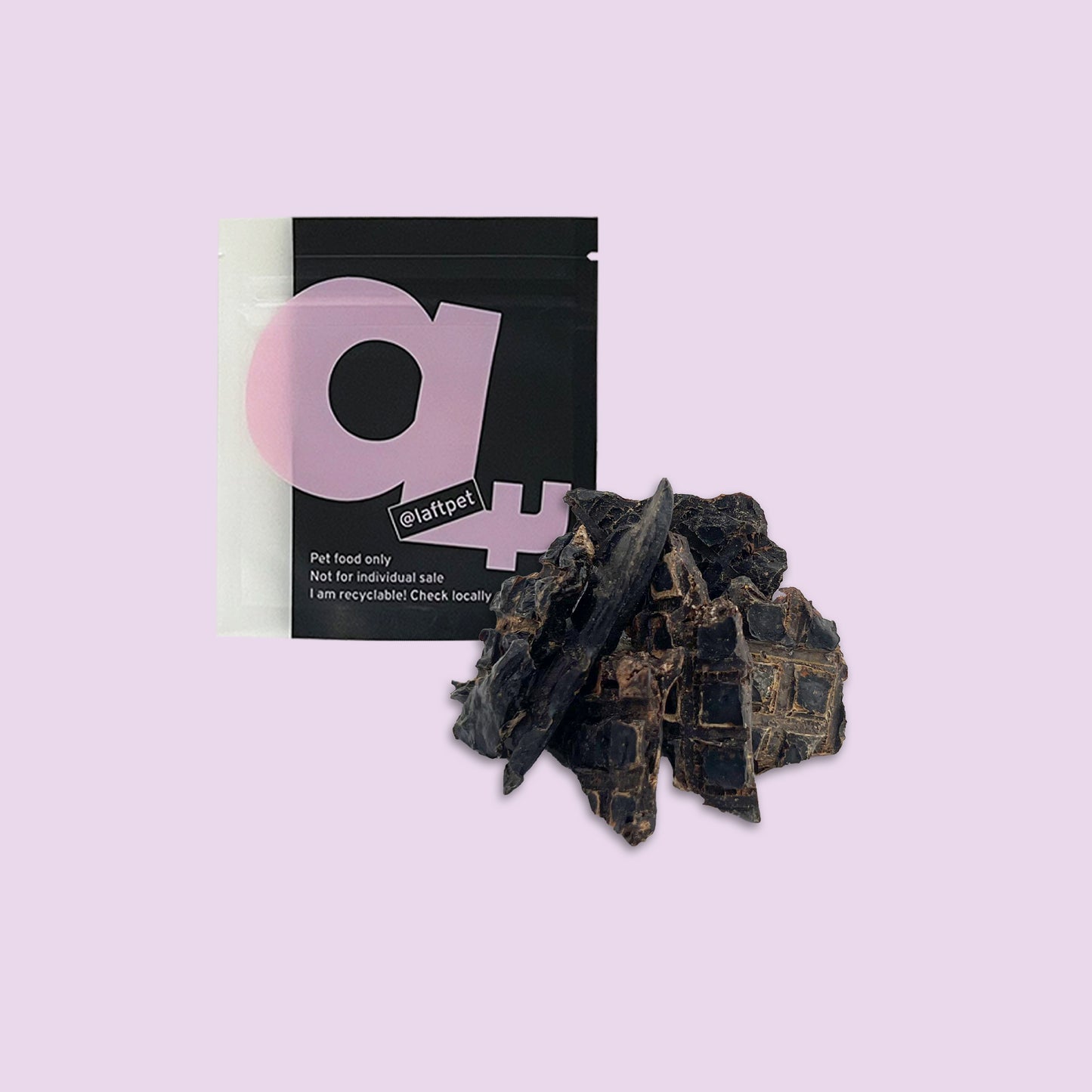 A black Laft Pet treat pouch placed next to a pile of dehydrated lamb liver dog treats on a light purple background.