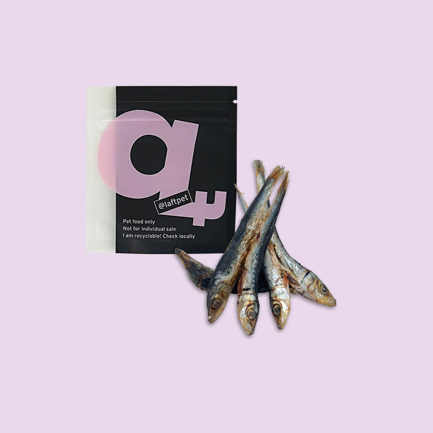 A black Laft Pet natural dog treat pouch placed next to a pile of dehydrated pilchards dog treats on a light purple background.