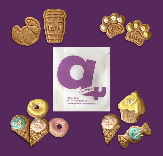 A variety decorated dog-friendly high tea biscuits, including croissants, coffee cups, paw prints, donuts, and cupcakes, displayed around a white Laft Pet pouch in a deep purple background.