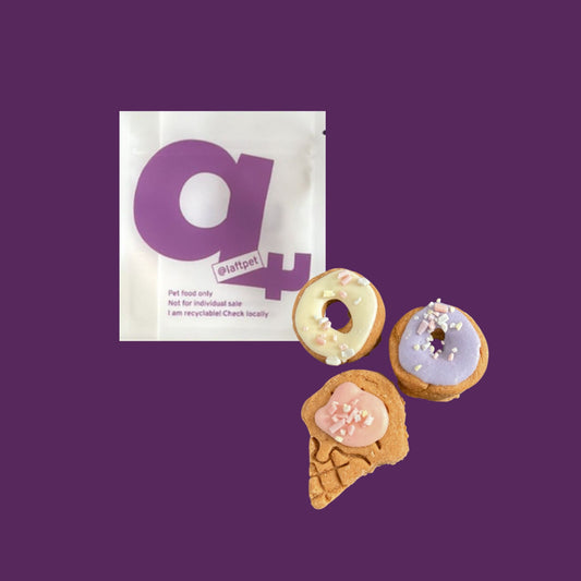 A white Laft Pet natural dog treat pouch placed next to two donuts and an ice-cream cookies on a dark purple background.