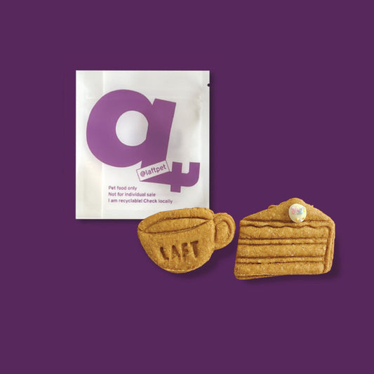 A white Laft Pet natural dog treat pouch placed next to a coffee cup and cake slice cookies on a dark purple background.