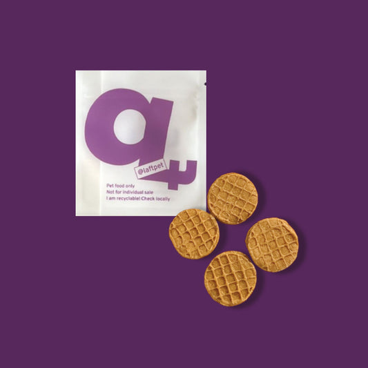 A white Laft Pet natural dog treat pouch placed next to mini waffle biscuits on a dark purple background.
