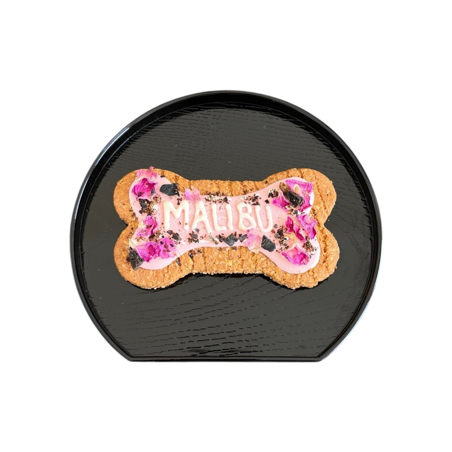 Personalised dog bone shaped biscuit, decorated with pink rose petals and pink icing with the name Malibu.