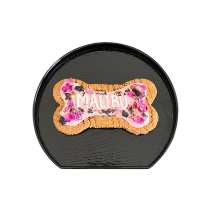 Personalised dog bone shaped biscuit, decorated with pink rose petals and pink icing with the name Malibu.