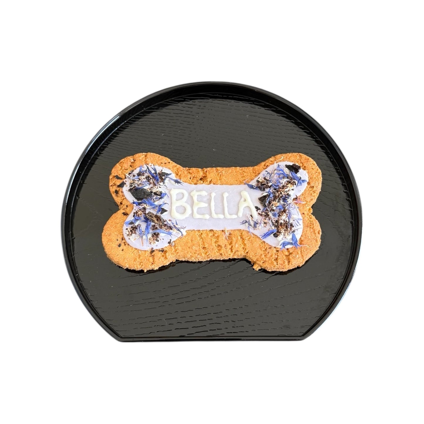 Personalised dog bone shaped biscuit, decorated with purple cornflowers and purple icing with the name Bella.