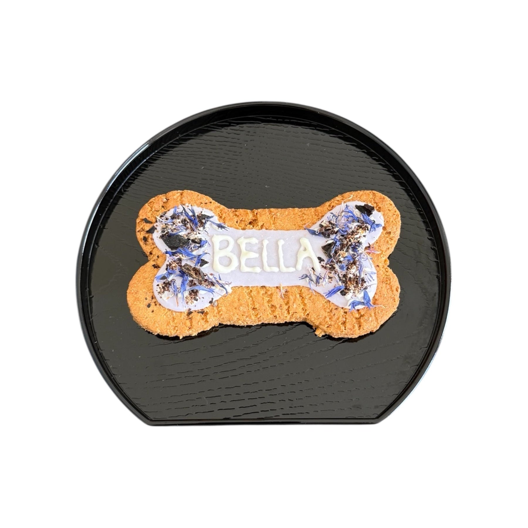 Personalised dog bone shaped biscuit, decorated with purple cornflowers and purple icing with the name Bella.