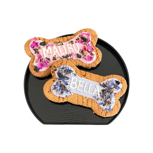 Two personalised dog bone shaped biscuit, decorated with flowers and icing with the names Malibu and Bella.