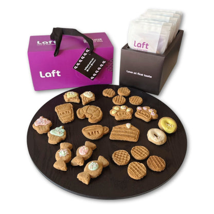 A presentation of the Laft Pet dog gift box. To the right, a sleek black container holds eight black-and-white pouches featuring the Laft logo and the tagline 'Love at first taste.' In the front, a round black serving platter displays various treats. The overall setup is clean, stylish, and visually appealing.