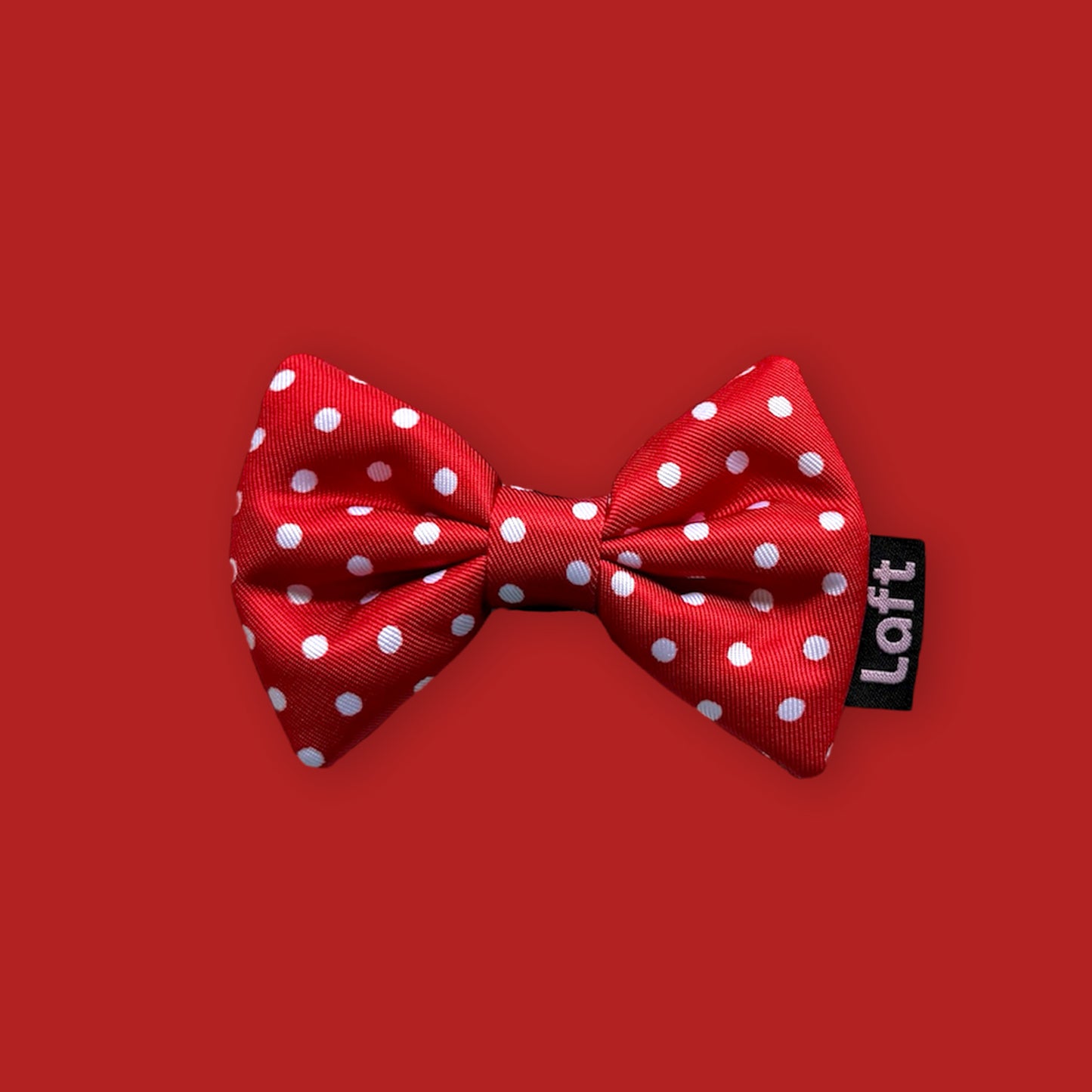 A red bow tie with white polka dots and a Laft label on the right displayed on a matching red background.