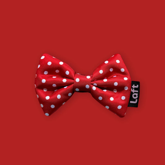 A red bow tie with white polka dots and a Laft label on the right displayed on a matching red background.