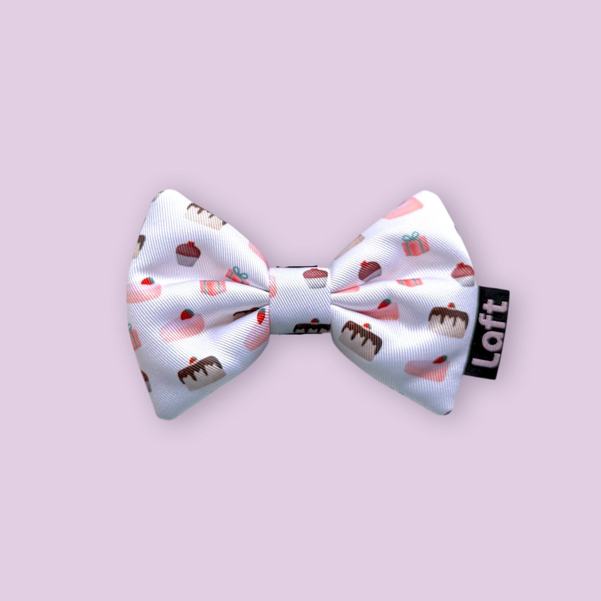 A white bow tie with dessert print and a Laft label on the right displayed on a light purple background.