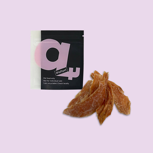 A black Laft Pet natural dog treat pouch placed next to a pile of dehydrated chicken jerky dog treats on a light purple background.