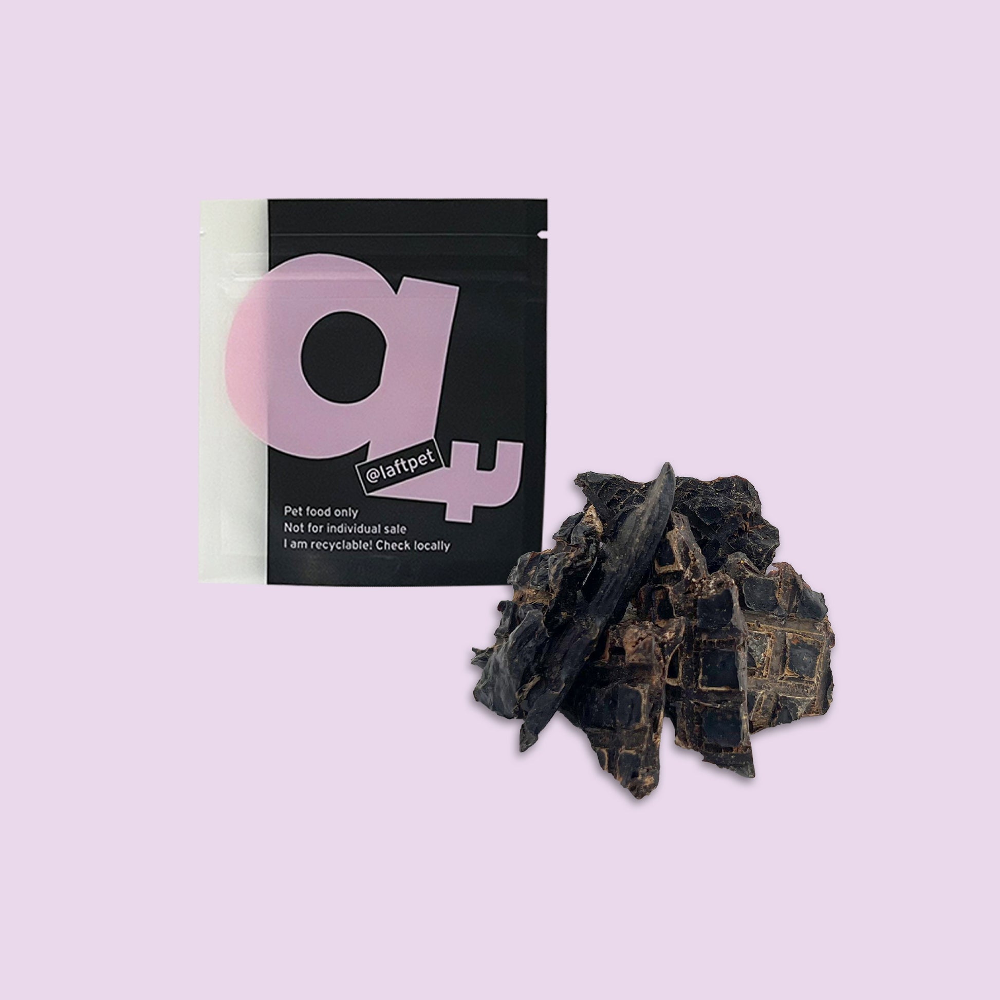 A black Laft Pet natural dog treat pouch placed next to a pile of dehydrated lamb liver dog treats on a light purple background.