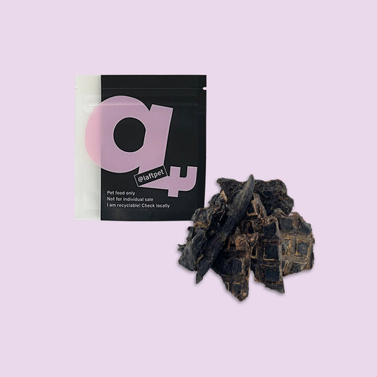 A black Laft Pet natural dog treat pouch placed next to a pile of dehydrated lamb liver dog treats on a light purple background.