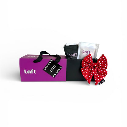A presentation of Laft Pet Dog Gift Box  including a purple box with Laft branding, black and white pouches with Laft's logo, and a red and white polka dot sailor bow on a white background.