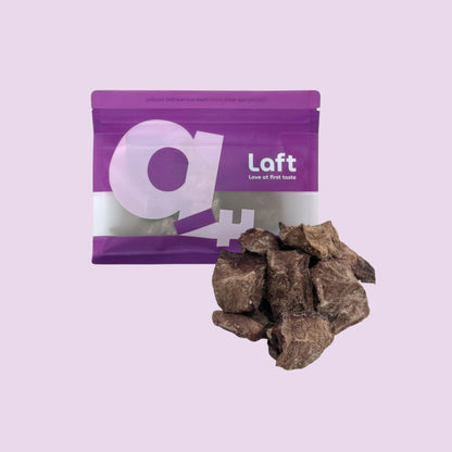 A purple Laft Pet natural dog treat pouch placed next to a pile of freeze-dried beef heart dog treats on a light purple background.