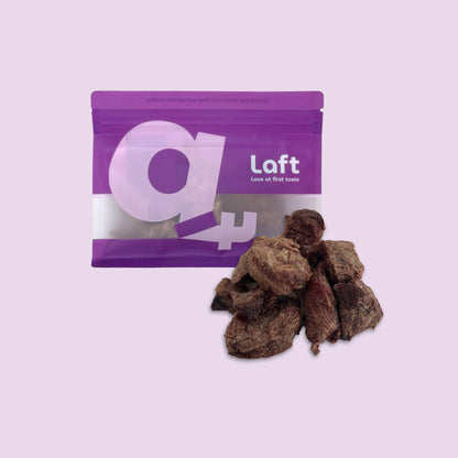 A purple Laft Pet natural dog treat pouch placed next to a pile of freeze-dried emu dog treats on a light purple background.