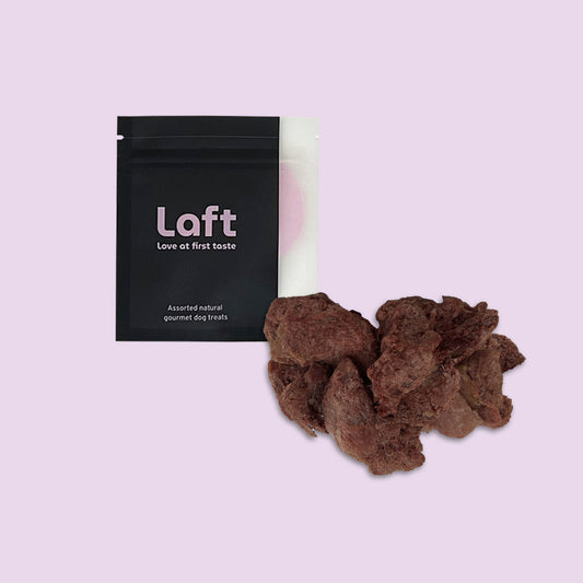A black Laft Pet natural dog treat pouch placed next to a pile of freeze-dried venison dog treats on a light purple background.