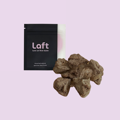 A black Laft Pet natural dog treat pouch placed next to a pile of freeze-dried venison dog treats on a light purple background.