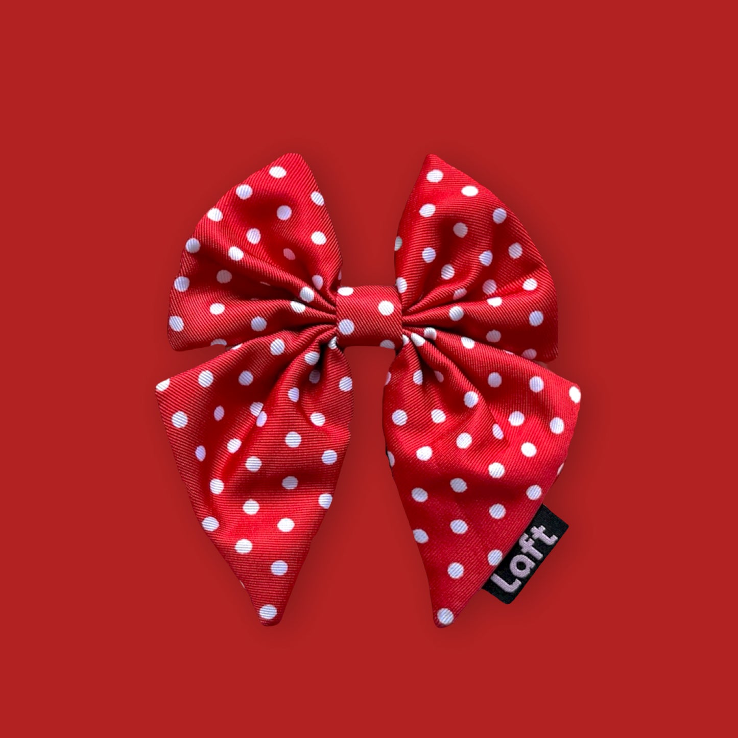 A red sailor bow with white polka dots and a Laft label on the right displayed on a matching red background.