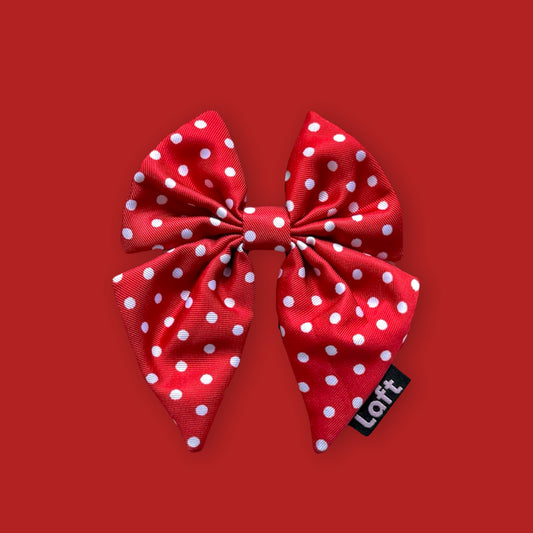 A red sailor bow with white polka dots and a Laft label on the right displayed on a matching red background.